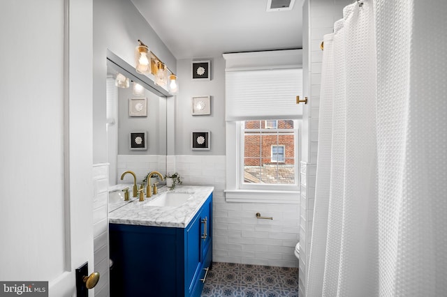 full bathroom featuring tile patterned flooring, a wainscoted wall, visible vents, vanity, and tile walls