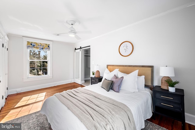 bedroom featuring ceiling fan, a barn door, wood finished floors, baseboards, and crown molding