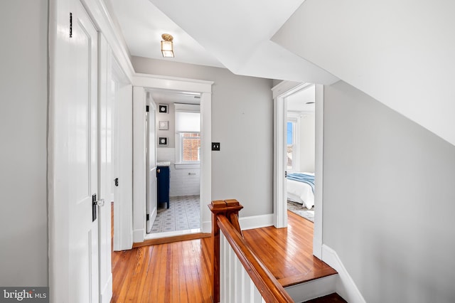 corridor with light wood-style floors, baseboards, and an upstairs landing