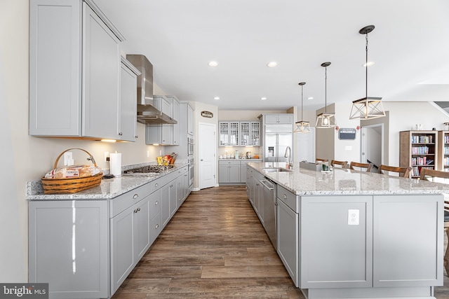 kitchen with a large island, wall chimney range hood, sink, hanging light fixtures, and stainless steel appliances