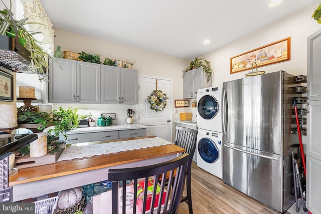 kitchen with light hardwood / wood-style flooring, stacked washer and clothes dryer, stainless steel refrigerator, and gray cabinets