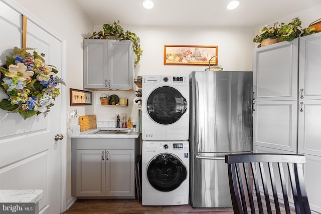 laundry area featuring dark hardwood / wood-style flooring, sink, and stacked washing maching and dryer