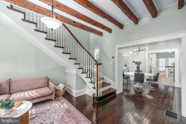 stairs featuring beam ceiling, hardwood / wood-style flooring, a chandelier, and a high ceiling