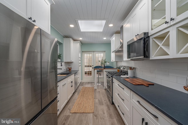 kitchen with tasteful backsplash, white cabinetry, sink, stainless steel appliances, and light hardwood / wood-style flooring