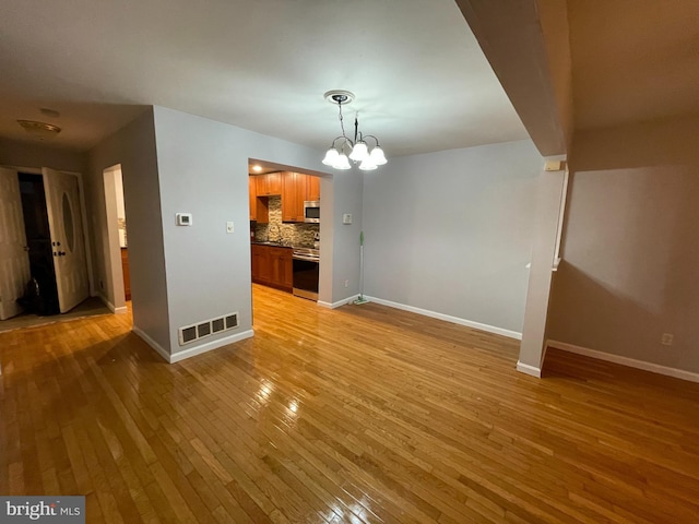 unfurnished living room featuring a notable chandelier and light wood-type flooring