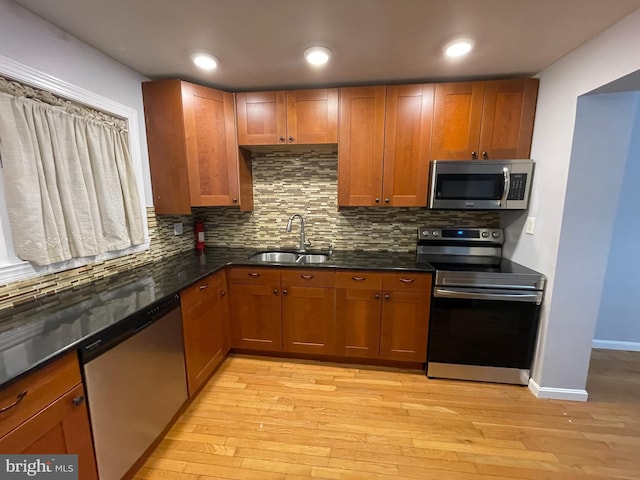 kitchen with tasteful backsplash, appliances with stainless steel finishes, sink, and light hardwood / wood-style floors