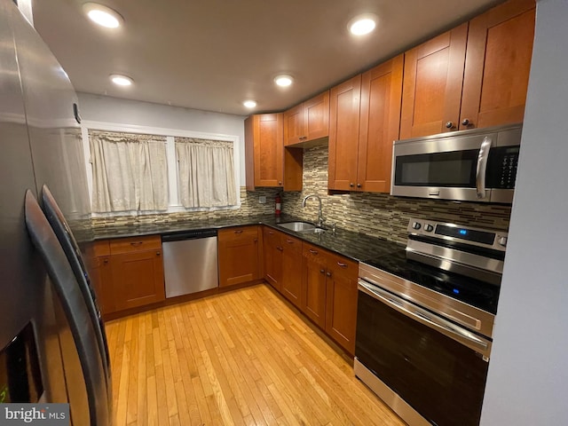 kitchen with sink, dark stone countertops, backsplash, stainless steel appliances, and light hardwood / wood-style floors