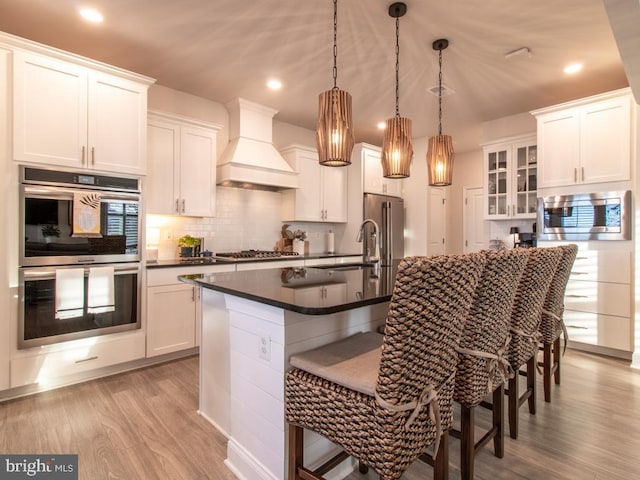 kitchen with white cabinetry, a breakfast bar area, custom exhaust hood, hanging light fixtures, and stainless steel appliances