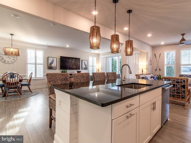 kitchen with sink, hardwood / wood-style flooring, white cabinetry, a kitchen island with sink, and decorative light fixtures