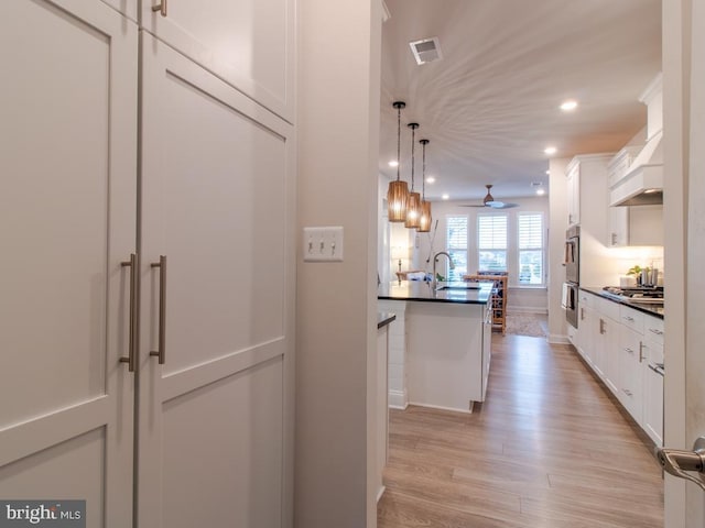 kitchen with pendant lighting, sink, light hardwood / wood-style floors, white cabinets, and custom exhaust hood