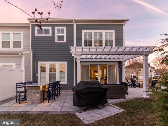 back house at dusk with a patio, an outdoor bar, and a pergola