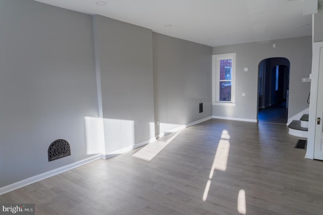 unfurnished room featuring arched walkways, visible vents, baseboards, and wood finished floors