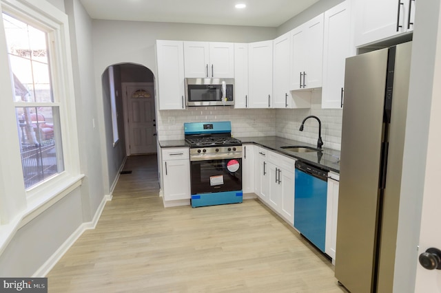 kitchen with light wood-style flooring, appliances with stainless steel finishes, arched walkways, white cabinets, and a sink