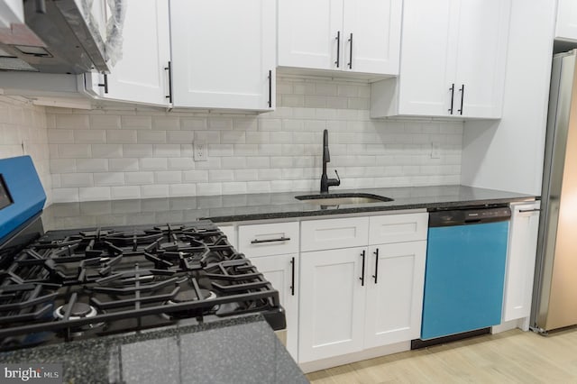 kitchen with light wood finished floors, dark stone counters, a sink, stainless steel appliances, and white cabinetry