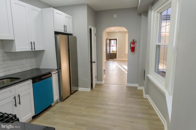 kitchen featuring freestanding refrigerator, arched walkways, white cabinets, light wood finished floors, and dishwashing machine