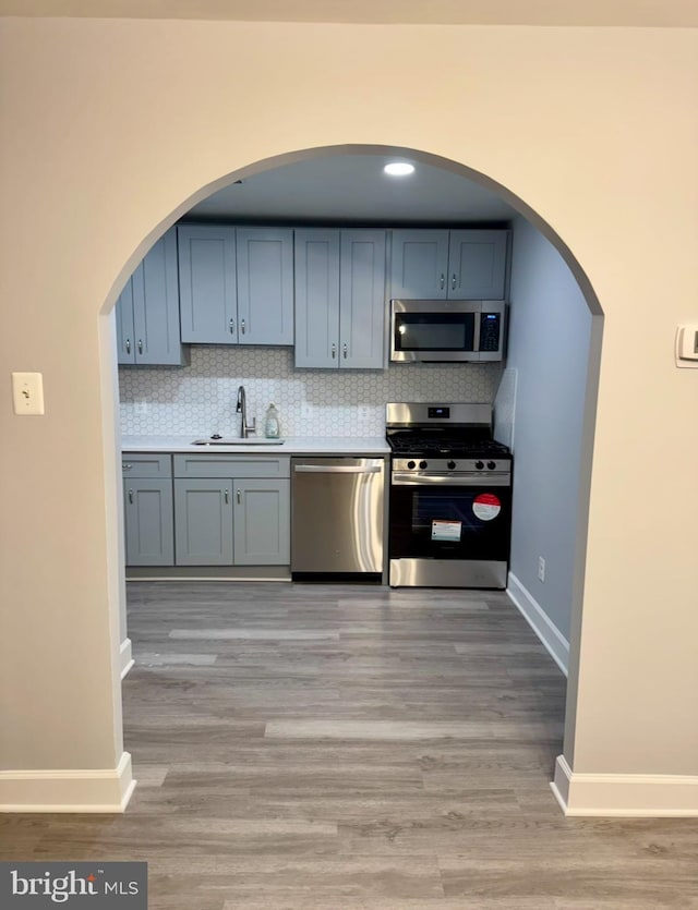 kitchen featuring appliances with stainless steel finishes, light hardwood / wood-style floors, sink, and backsplash