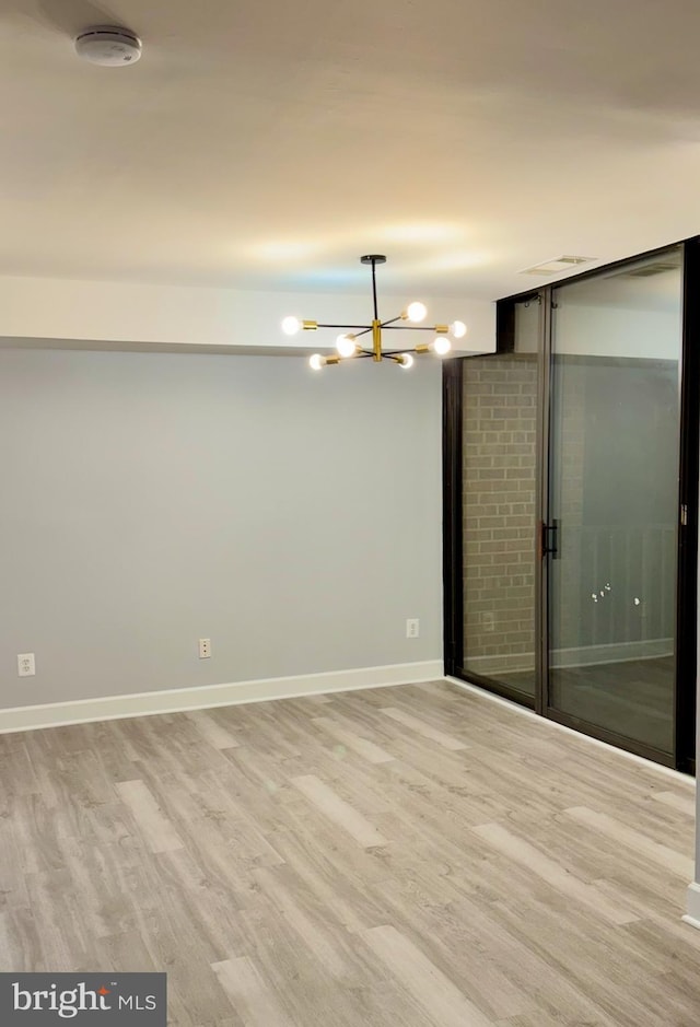 empty room with a notable chandelier and light hardwood / wood-style floors