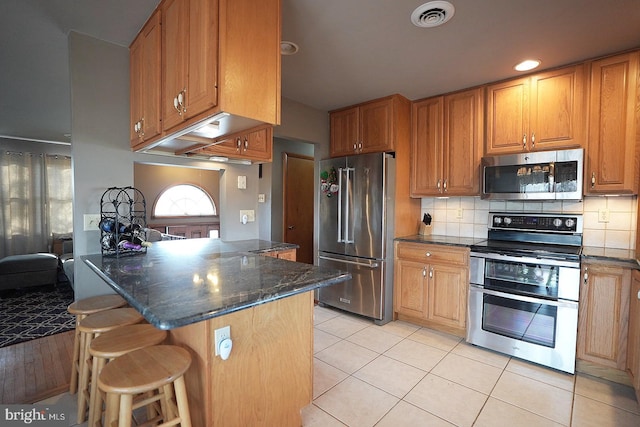 kitchen with a breakfast bar, stainless steel appliances, tasteful backsplash, kitchen peninsula, and dark stone counters