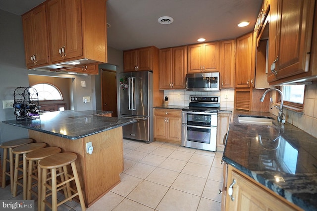 kitchen with appliances with stainless steel finishes, sink, a breakfast bar area, dark stone countertops, and light tile patterned floors