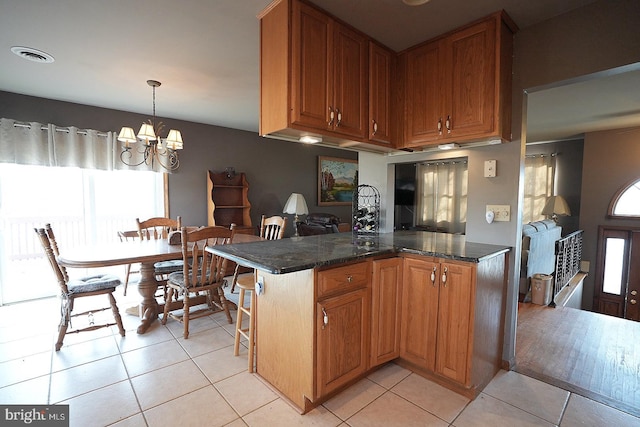 kitchen with dark stone countertops, an inviting chandelier, light tile patterned flooring, decorative light fixtures, and kitchen peninsula