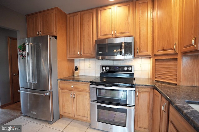 kitchen featuring tasteful backsplash, stainless steel appliances, dark stone counters, and light tile patterned flooring