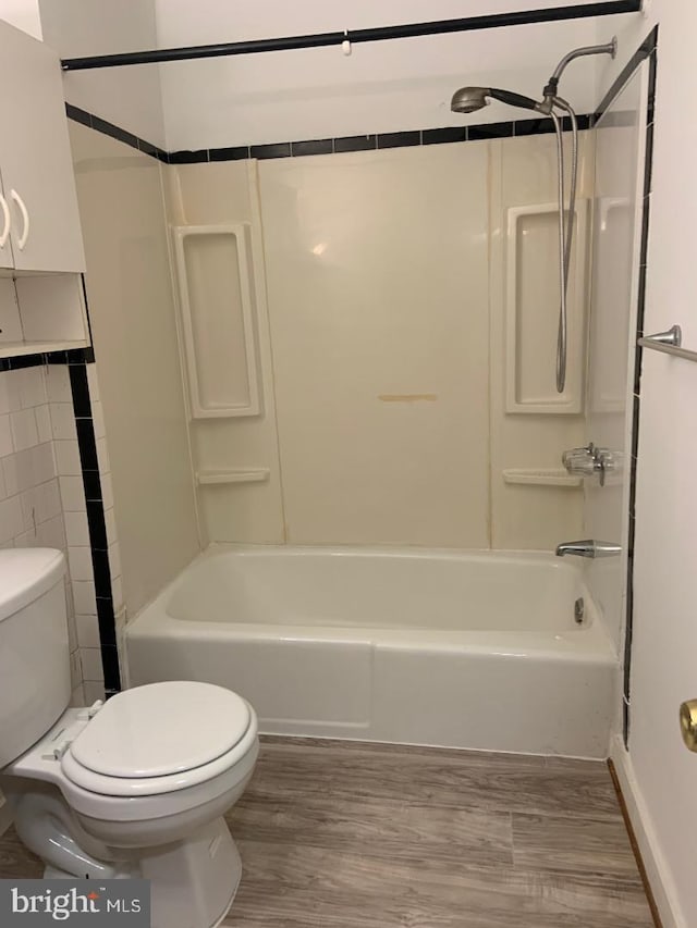 bathroom featuring tile walls, hardwood / wood-style floors, bathing tub / shower combination, and toilet