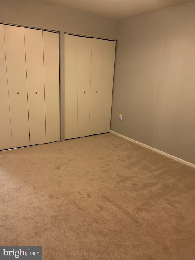 unfurnished bedroom with two closets and light colored carpet