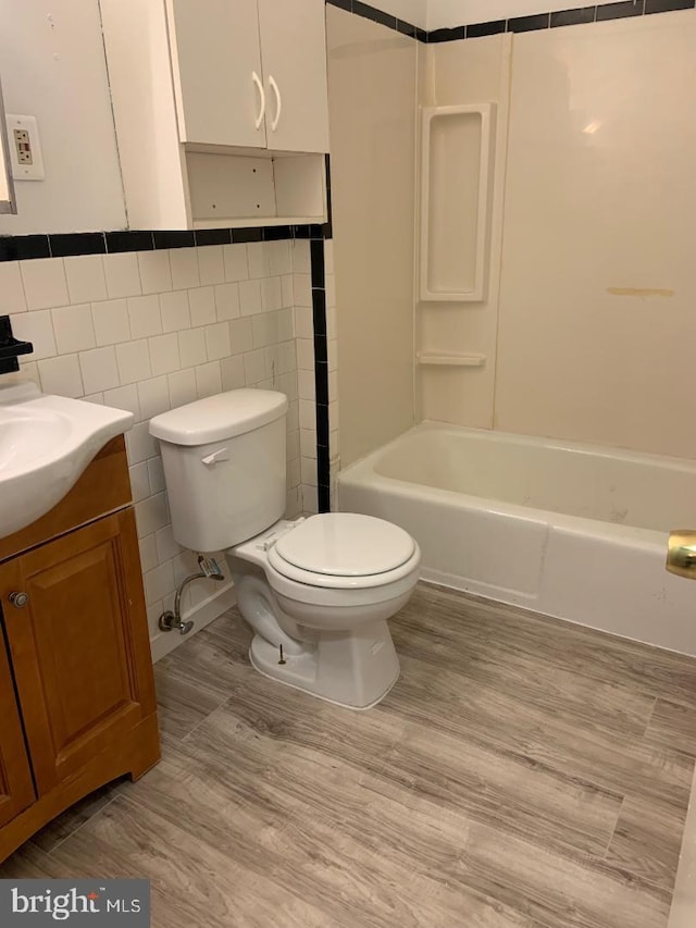 full bathroom with  shower combination, tile walls, vanity, wood-type flooring, and toilet