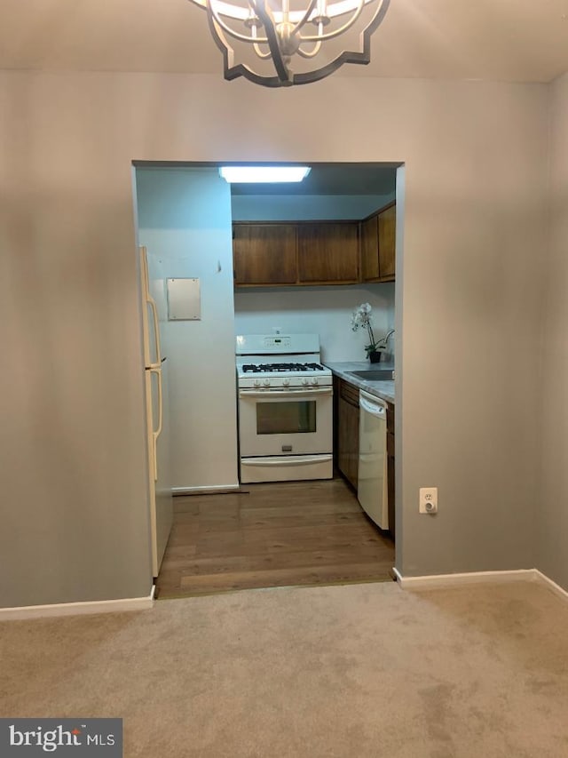 kitchen featuring sink, white appliances, dark brown cabinets, light carpet, and a chandelier