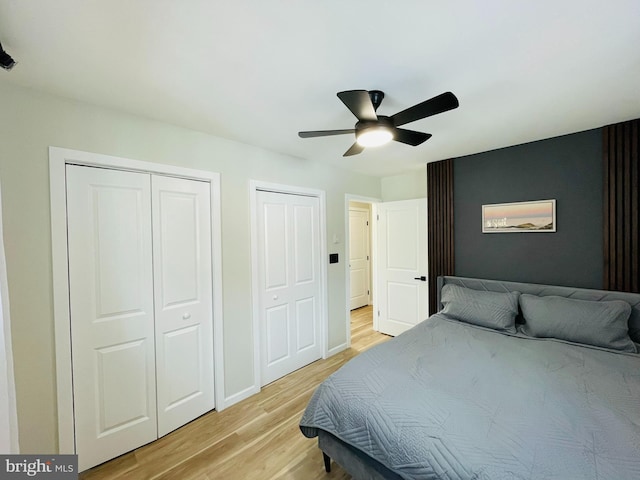 bedroom with ceiling fan, light hardwood / wood-style floors, and multiple closets