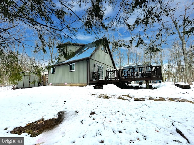 snow covered back of property featuring a wooden deck and a storage unit