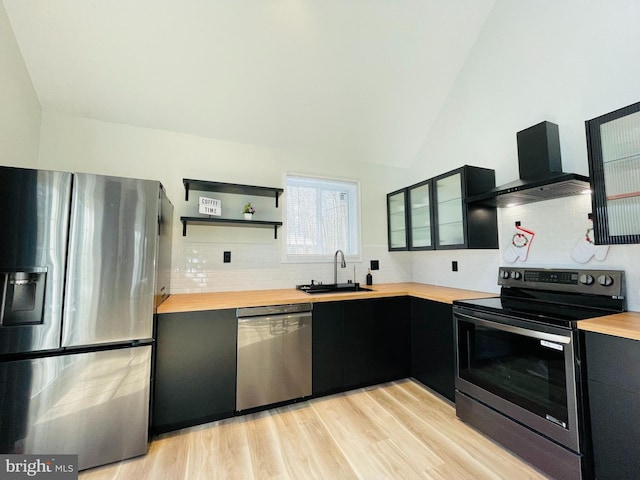 kitchen with wood counters, wall chimney exhaust hood, sink, light wood-type flooring, and appliances with stainless steel finishes