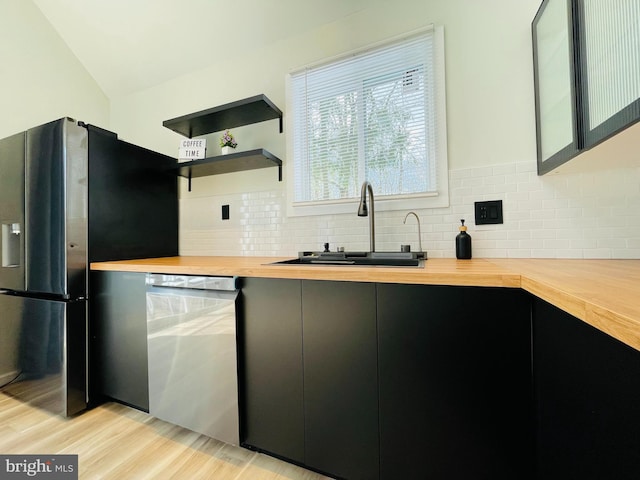 kitchen featuring butcher block countertops, tasteful backsplash, sink, dishwashing machine, and stainless steel refrigerator with ice dispenser