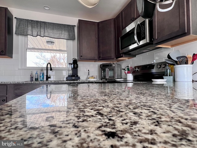 kitchen with light stone counters, appliances with stainless steel finishes, dark brown cabinets, and backsplash