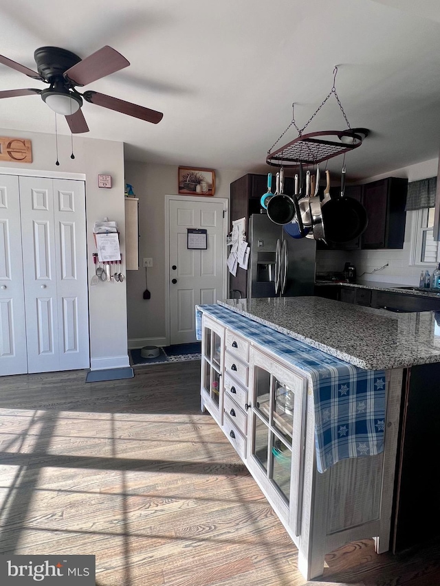 kitchen featuring dark brown cabinetry, stainless steel fridge with ice dispenser, wood-type flooring, and stone countertops