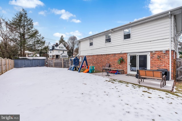 snow covered back of property featuring a patio and a playground