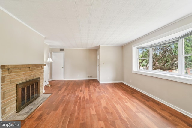 unfurnished living room with wood finished floors, visible vents, crown molding, baseboards, and a glass covered fireplace