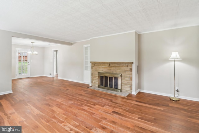 unfurnished living room with baseboards, a notable chandelier, wood finished floors, a stone fireplace, and ornamental molding