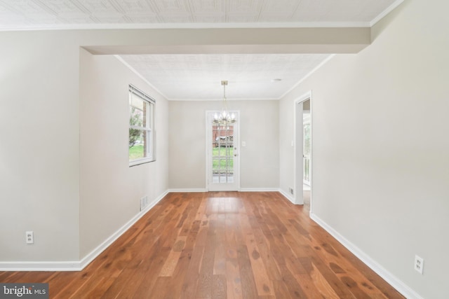 unfurnished dining area featuring hardwood / wood-style flooring, baseboards, crown molding, and a chandelier