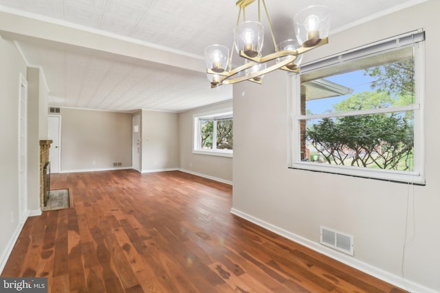 empty room featuring baseboards, visible vents, a notable chandelier, wood finished floors, and crown molding