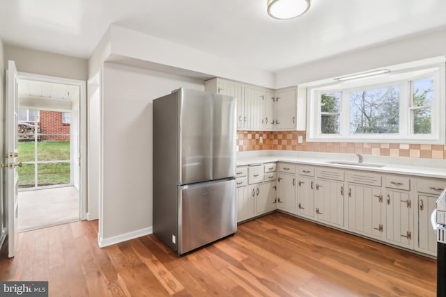 kitchen featuring a sink, tasteful backsplash, light wood-type flooring, freestanding refrigerator, and light countertops