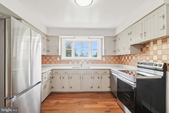 kitchen featuring light countertops, wood finished floors, a sink, tasteful backsplash, and appliances with stainless steel finishes