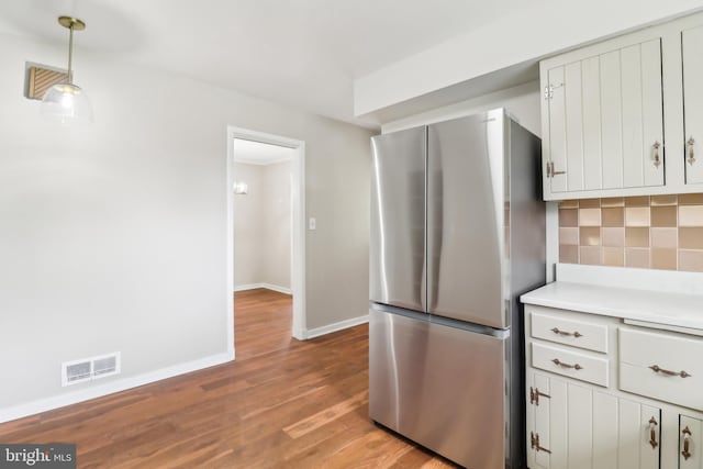 kitchen featuring backsplash, wood finished floors, visible vents, freestanding refrigerator, and baseboards