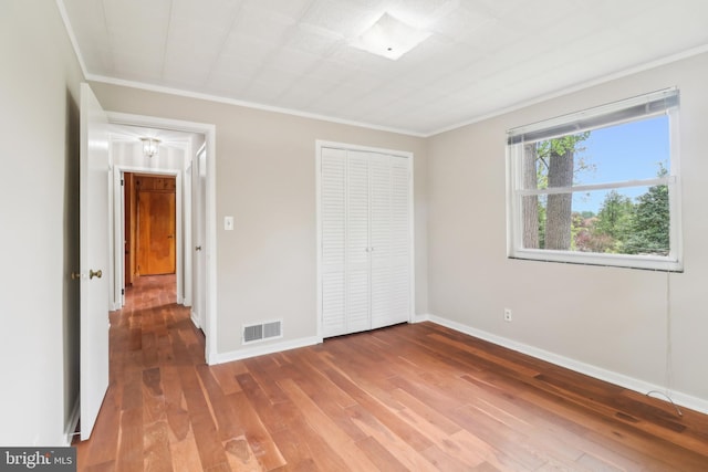 unfurnished bedroom featuring hardwood / wood-style floors, baseboards, visible vents, and ornamental molding