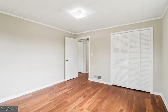 unfurnished bedroom featuring baseboards, wood finished floors, visible vents, and a closet