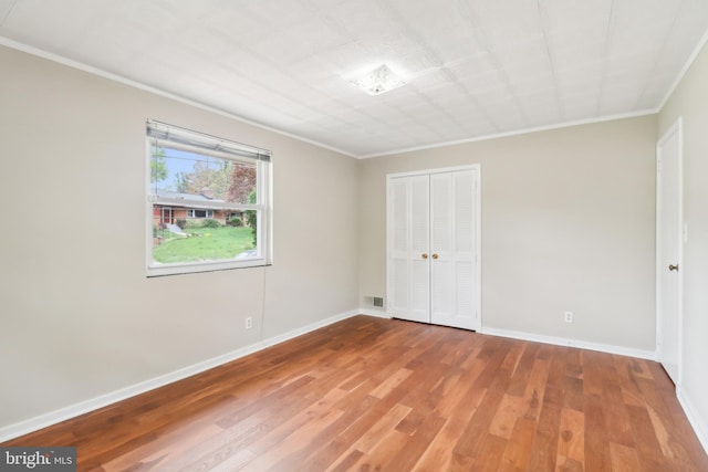 unfurnished bedroom featuring baseboards, wood finished floors, a closet, and crown molding