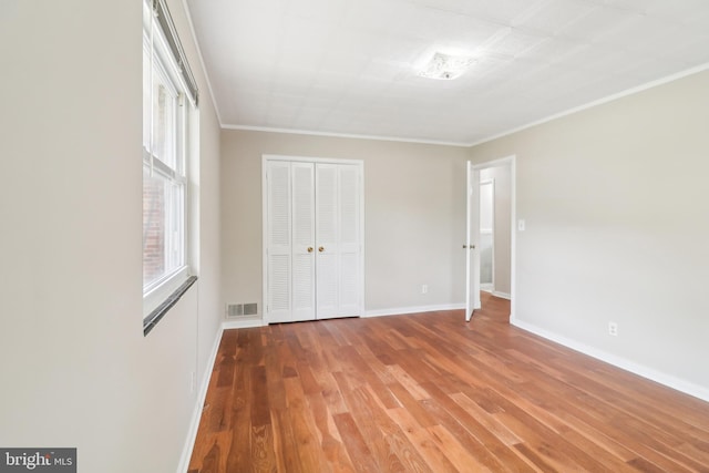 unfurnished bedroom with visible vents, baseboards, wood finished floors, a closet, and ornamental molding