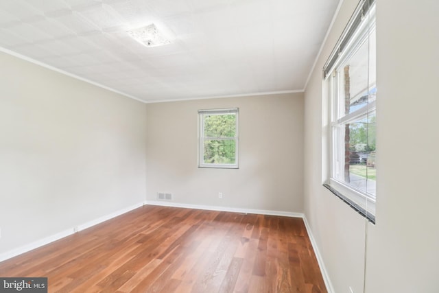 unfurnished room with baseboards, wood finished floors, visible vents, and crown molding