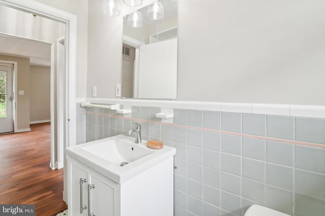 half bath featuring wood finished floors, visible vents, vanity, tile walls, and wainscoting