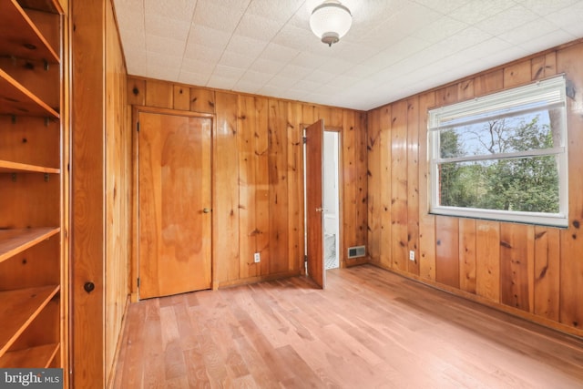 unfurnished bedroom featuring wood walls, wood finished floors, visible vents, and baseboards